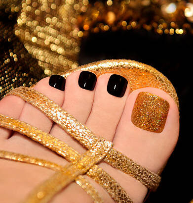 Luxury pedicure with black and gold lacquer on women's toes on the black and brilliant background.